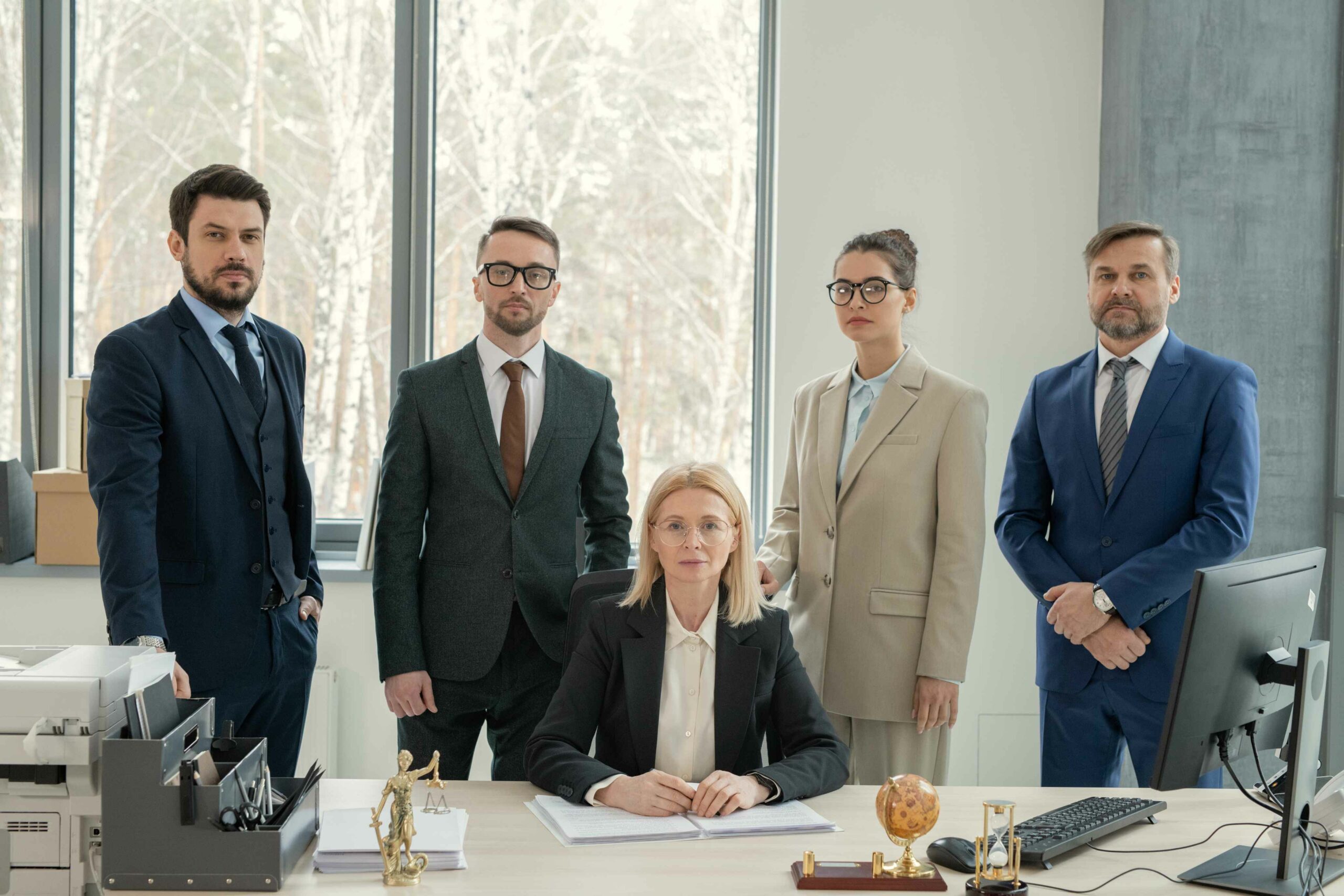 serious-mature-female-chef-law-firm-surrounded-by-lawyers-sitting-with-documents-desk-modern-office (1)